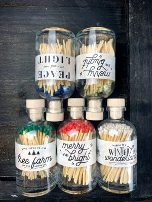 Set of six vintage apothecary match jars in festive holiday colors and labels, displayed on a dark wood surface.