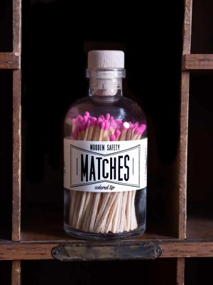 Vintage Apothecary Pink Matches in a glass jar with a cork top, with pink match tips, displayed on a wooden shelf. The label says 'Wooden Safety Matches' in black and white.