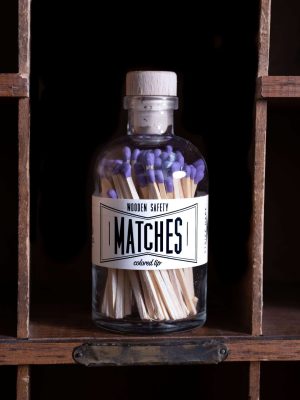 Vintage Apothecary Purple Matches in a glass jar with a cork top, with purple match tips, displayed on a wooden shelf. The label reads 'Wooden Safety Matches' in black and white.