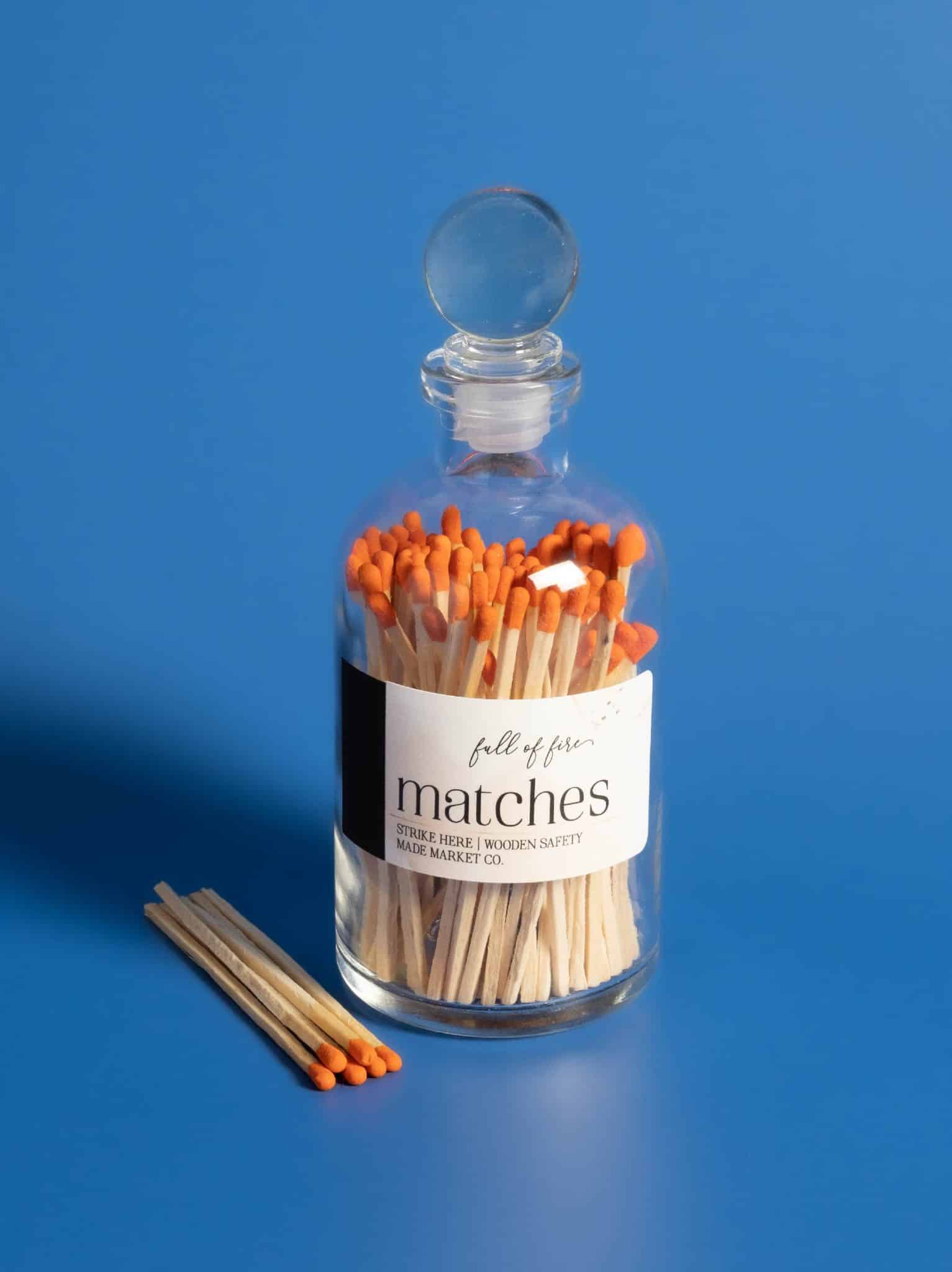Glass jar of Full of Fire Matches with orange match tips on a blue background
