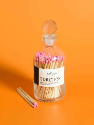 Glass jar of Full of Fire Matches with pink match tips on an orange background