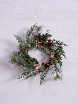 Holiday wreath with pine needles, red berries, and natural pinecones on a white wall.