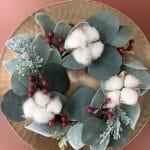 Holiday wreath with faux cotton, eucalyptus, and berries styled on a gold charger plate.