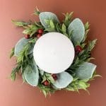 Holiday wreath with green leaves and red berries wrapped around a white candle, viewed from above.