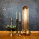 Brass Taper Candle Holders with holiday décor, including holly and berries, alongside a brass tray and ball ornament, displayed in a cozy setting.