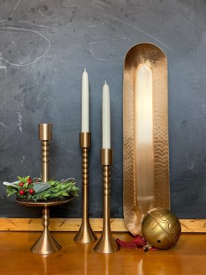 Brass Taper Candle Holders with holiday décor, including holly and berries, alongside a brass tray and ball ornament, displayed in a cozy setting.