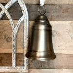 Small brass bell with rope loop hanging from a wall hook.