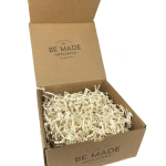 Open kraft gift box with ivory crinkle paper and Be Made Mercantile branding on the lid and front.