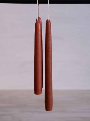 Clay taper candles in a terracotta color, shown hanging with a hand-dipped finish.