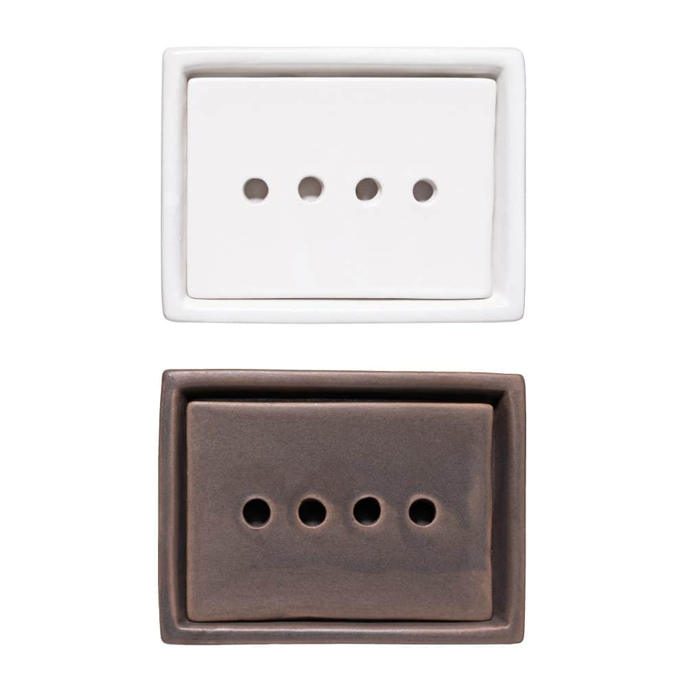 Top view of two stoneware soap dishes with four drainage holes, one in matte white and one in dark brown.