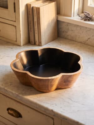 Angled side view of the Black Scalloped Bowl showing the carved wood sitting on a kitchen countertop.