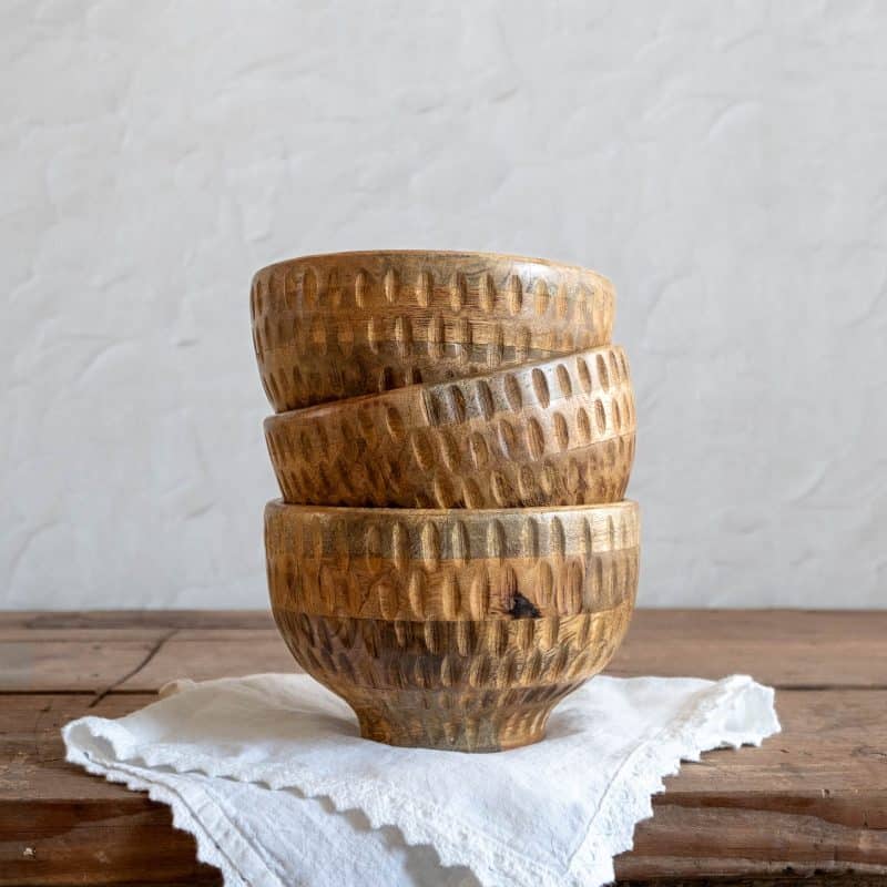 Stack of three Textured Wood Footed Bowls on a white linen cloth over a rustic wood surface