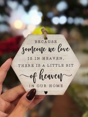 Hexagon “Someone We Love Is in Heaven” ornament held in hand with twine hanger and black script lettering.