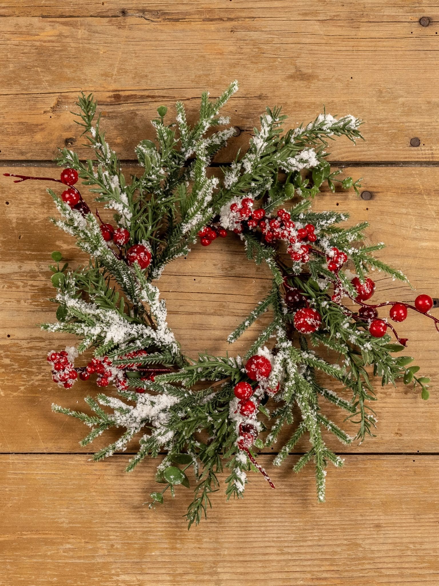 Snowy Evergreen Berry Candle Ring displayed flat, highlighting the snow-tipped evergreens and vibrant red berries.