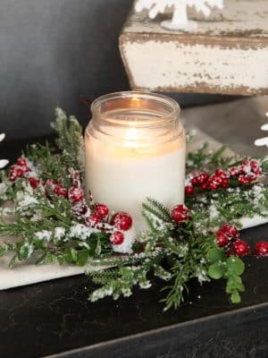 Snowy Evergreen Berry Candle Ring styled around a jar candle, showing frosted greenery and bright red berries.