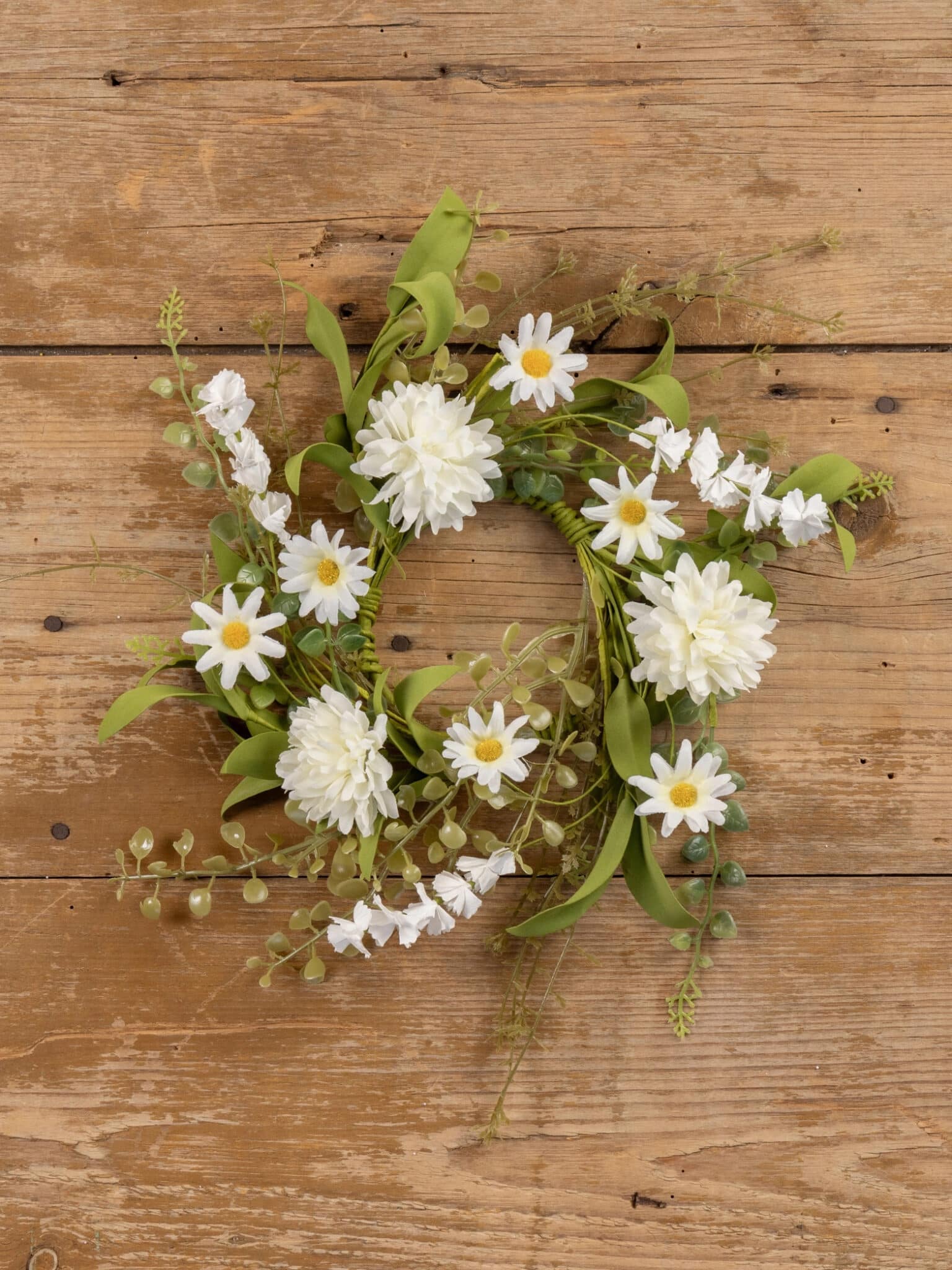 White Pom Pom Wildflower Candle Ring, 12-inch, featuring white pom pom flowers, daisy-style blooms, and layered greenery on a rustic wood surface.