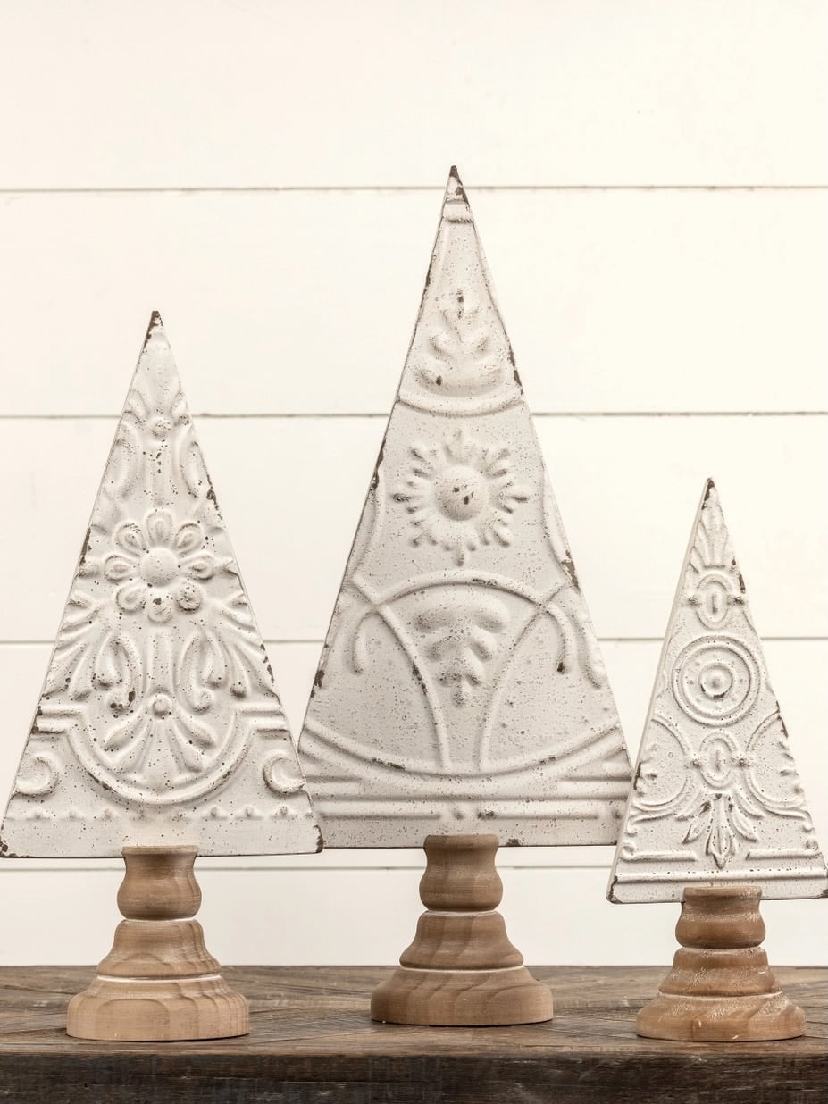 Antique white pressed metal Christmas trees with natural wood bases, embossed detailing, and a vintage-inspired distressed finish.