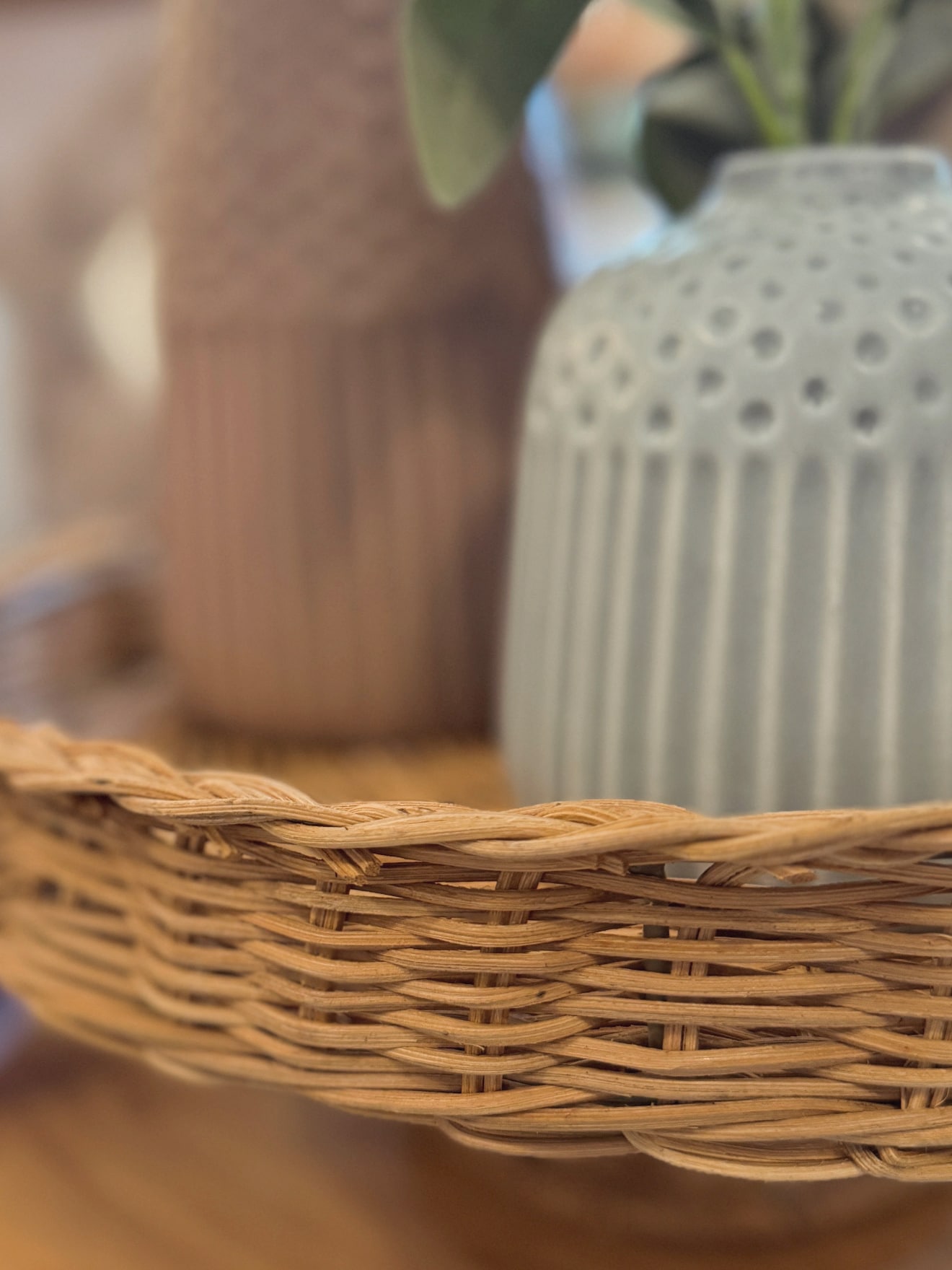 Close-up of woven rattan pedestal edge showing braided rim and natural fibers with decorative vases in the background.