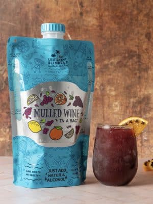Blue pouch labeled “Mulled Wine in a Bag” displayed beside a glass of mulled wine with orange slice garnish.