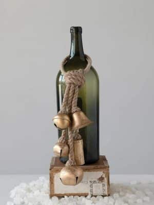 Set of Hanging Gold Bells with natural jute rope displayed over a green glass bottle for a simple, rustic holiday accent.