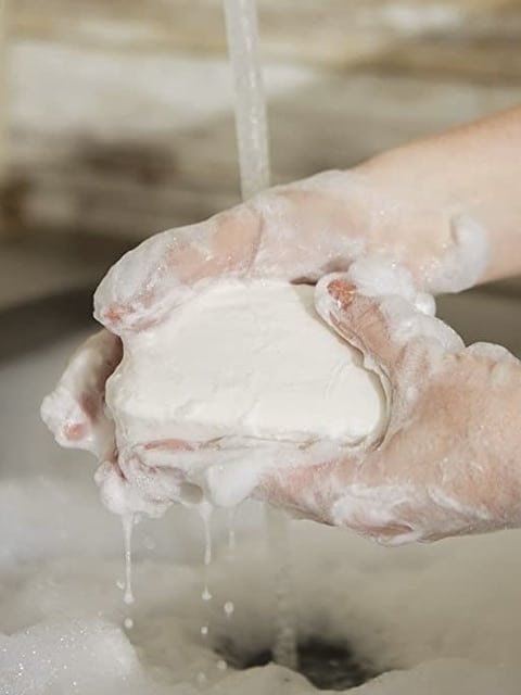 Hands lathering the Pré de Provence Milk Soap bar under running water, showing creamy texture