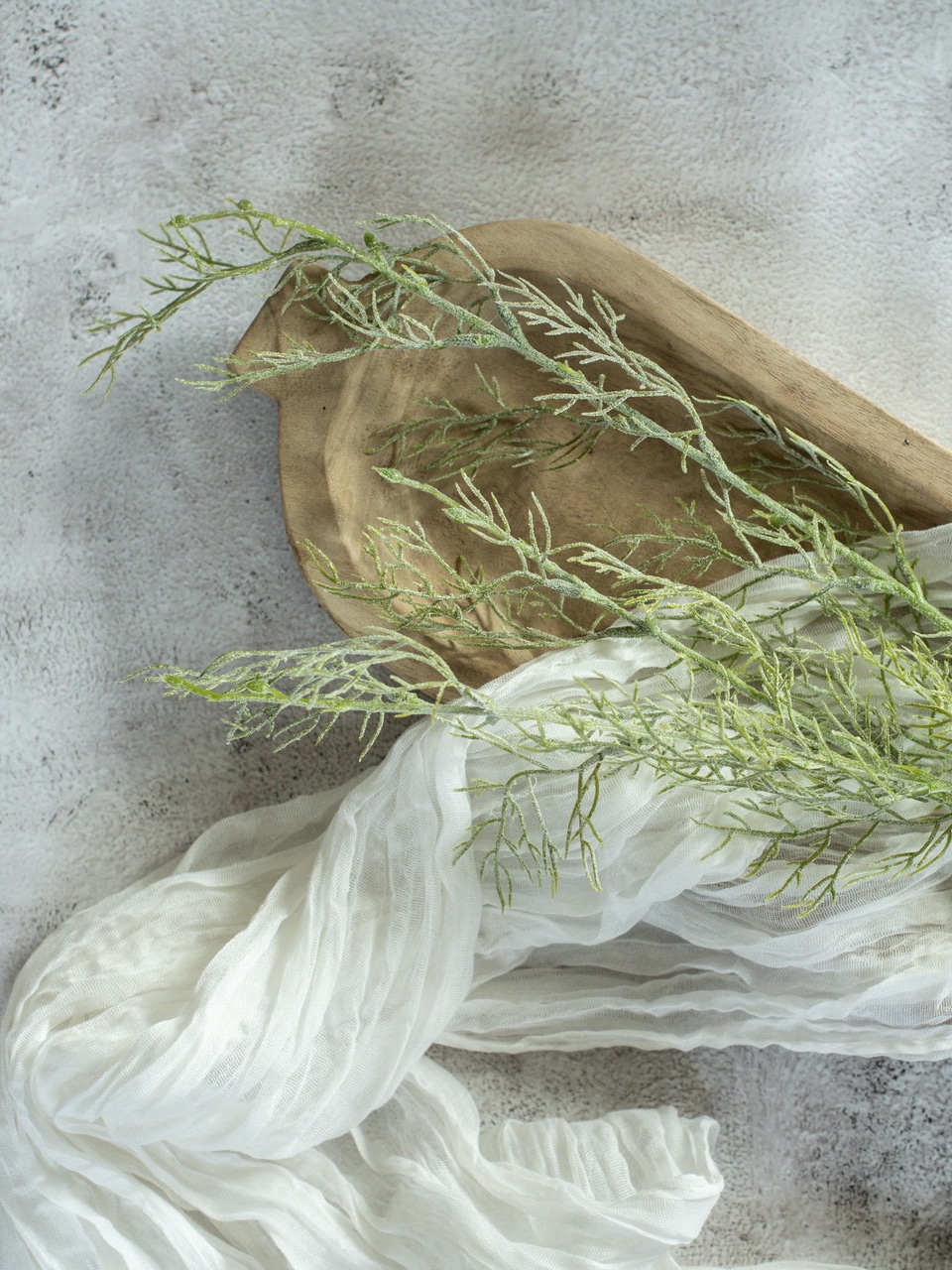 Realistic faux asparagus greenery stem styled in neutral vase beside candles and vintage books.
