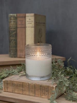 Clear 5-inch Dotted Glass Flameless Candle displayed beside vintage books, showing its warm ambient glow and textured dotted glass.
