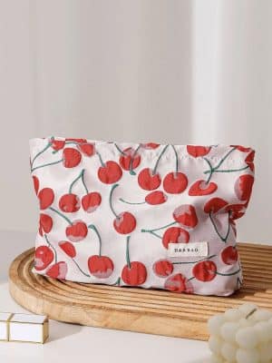 Large padded makeup bag with red cherry print and beige cotton lining, styled on a wooden tray.