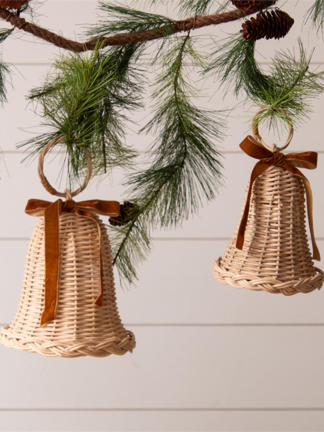 Rattan bells hanging from greenery with brown velvet bows for holiday decor.
