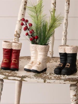 Red, white, and black ceramic Santa boot vases styled together, with one filled with greenery and berries.