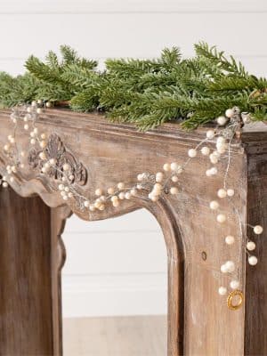 Silver and gold beaded garland draped across carved wood mantel with greenery.