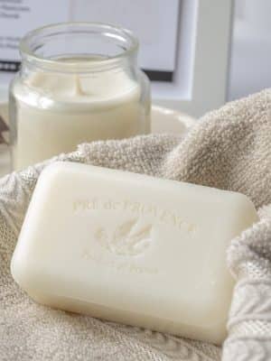 Pré de Provence Milk Bar Soap resting on a beige towel beside a lit candle in a cozy bathroom setting