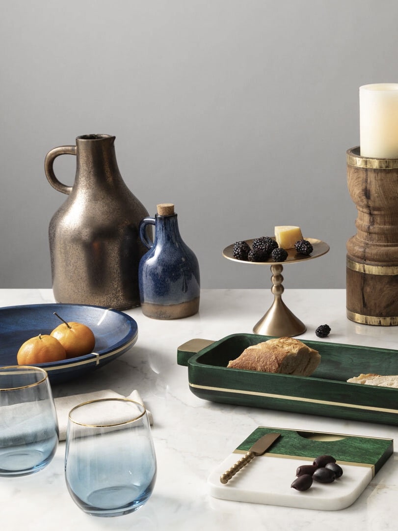 Elegant tabletop scene with ceramic pitchers, a brass pedestal, emerald green wood serveware, and a marble board.
