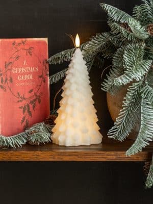 Cream 3D fir tree flameless candle styled on a shelf with Christmas décor and greenery