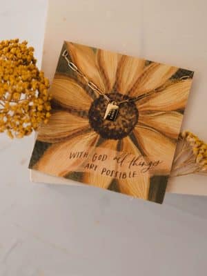 Gold mini tag necklace on sunflower card with engraved scripture message, styled with yellow florals.