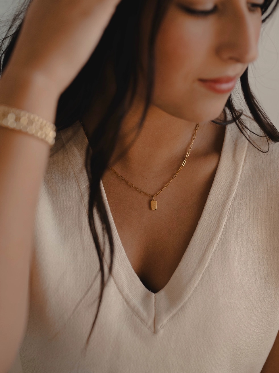 Woman wearing gold mini tag necklace engraved with “All Things” and “Phil. 4:13.”