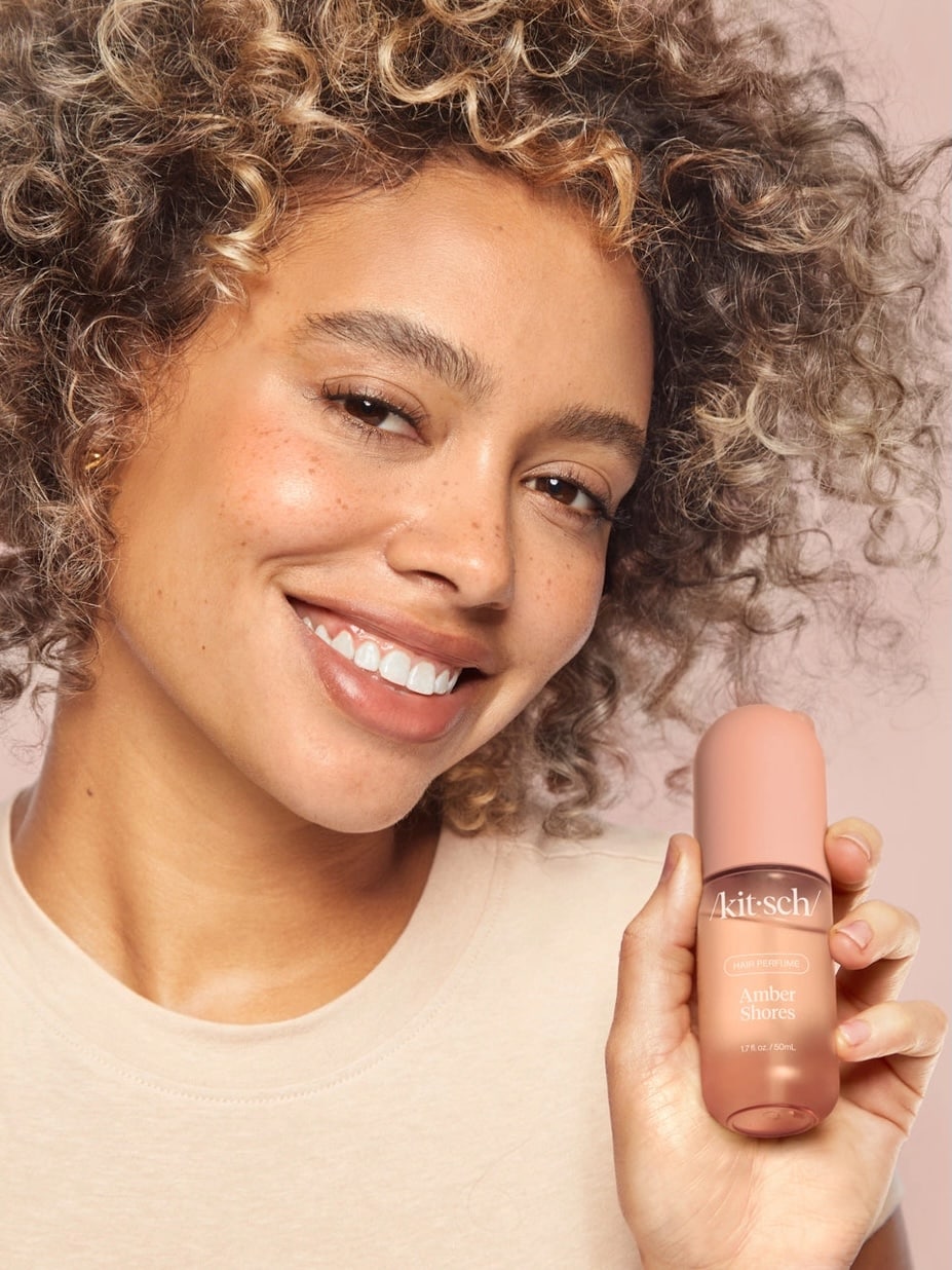 Kitsch Amber Shores Hair Perfume bottle with warm-toned background and natural elements like driftwood and amber stones.