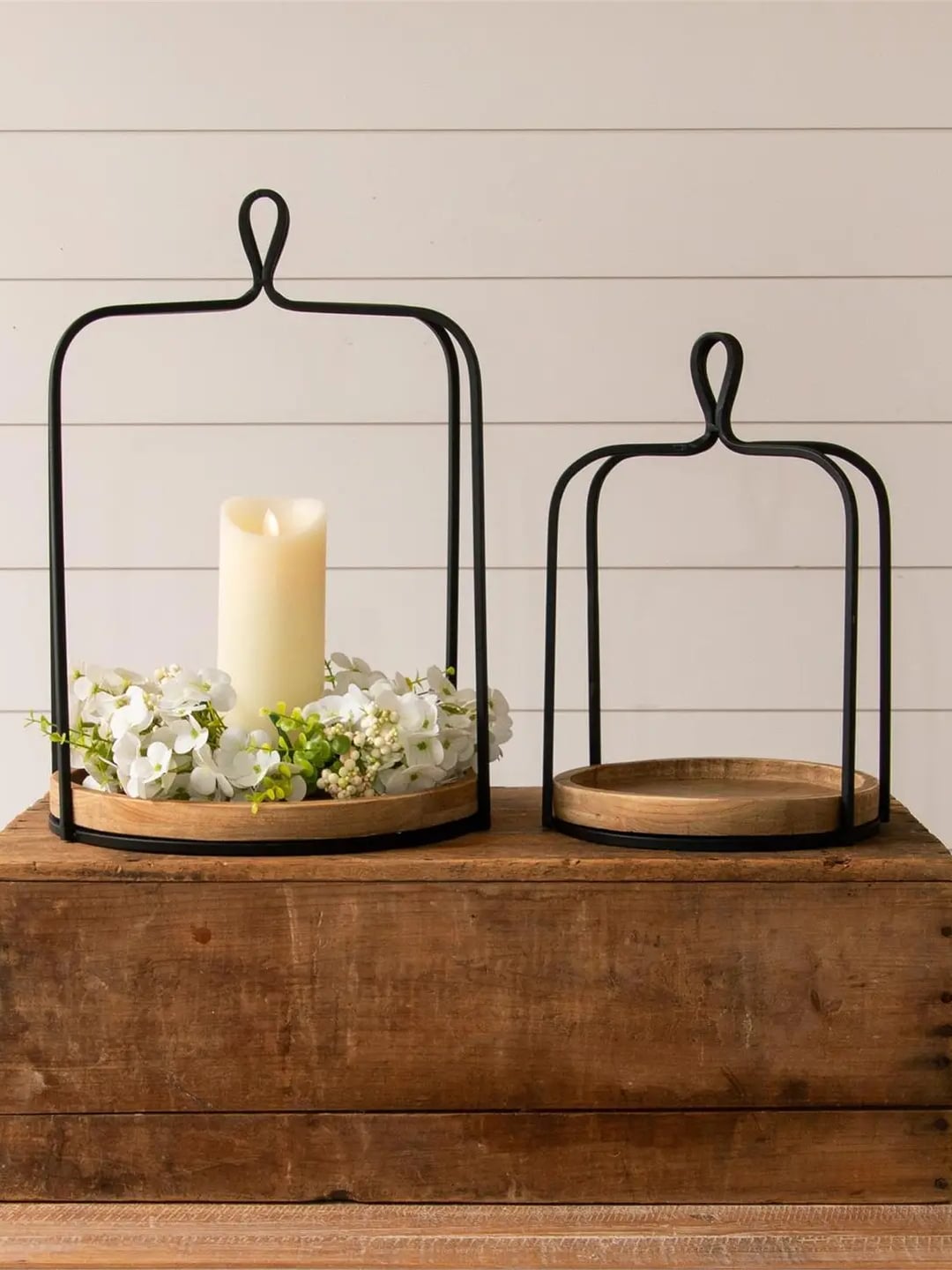 Black metal open frame lantern with a pillar candle and white florals styled on a wooden base.