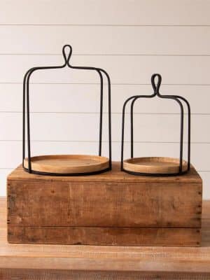 Set of two black metal open frame lanterns with round natural wood bases displayed on a rustic wooden box.