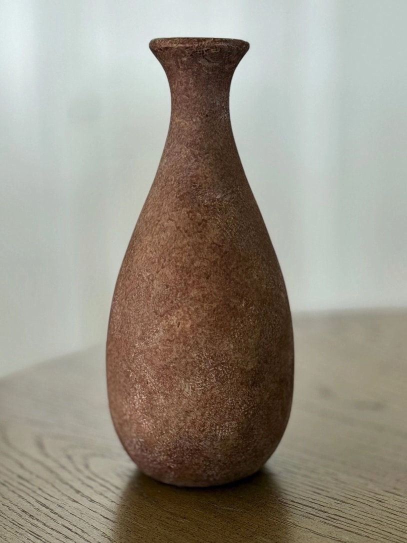 Close-up of a tall, narrow clay vase in a warm brown finish with subtle texture and handcrafted appearance.