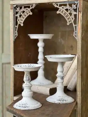 Cream distressed pillar candle holders in three different heights displayed together on a rustic wooden shelf, styled with vintage books.
