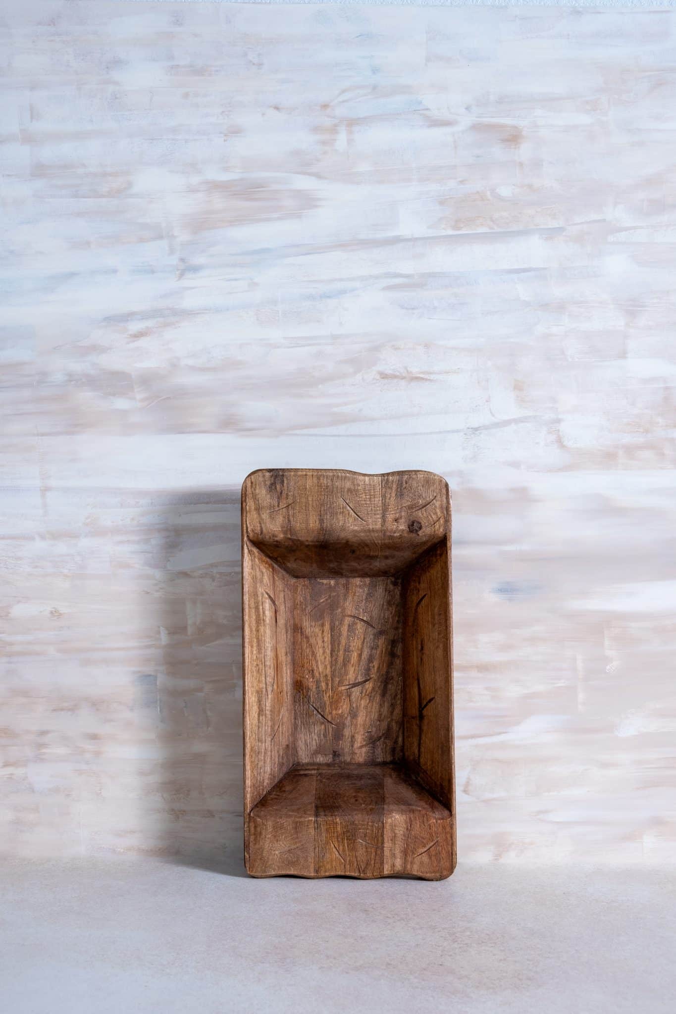 Small hand-carved wooden dough bowl with natural finish, standing upright against a textured light-toned background.
