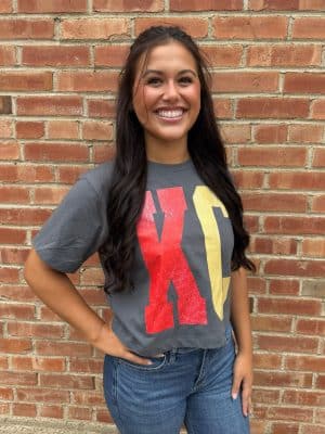 Woman wearing Pepper-colored long crop KC tee with bold red and gold block lettering.