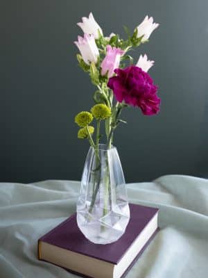 Faceted frosted glass vase with pink and purple flowers, styled on a purple book with a soft fabric backdrop.