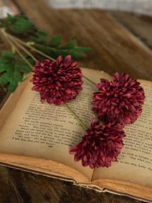 Burgundy Pom Pom Spray with lifelike blooms styled on an open vintage book for cozy seasonal décor.