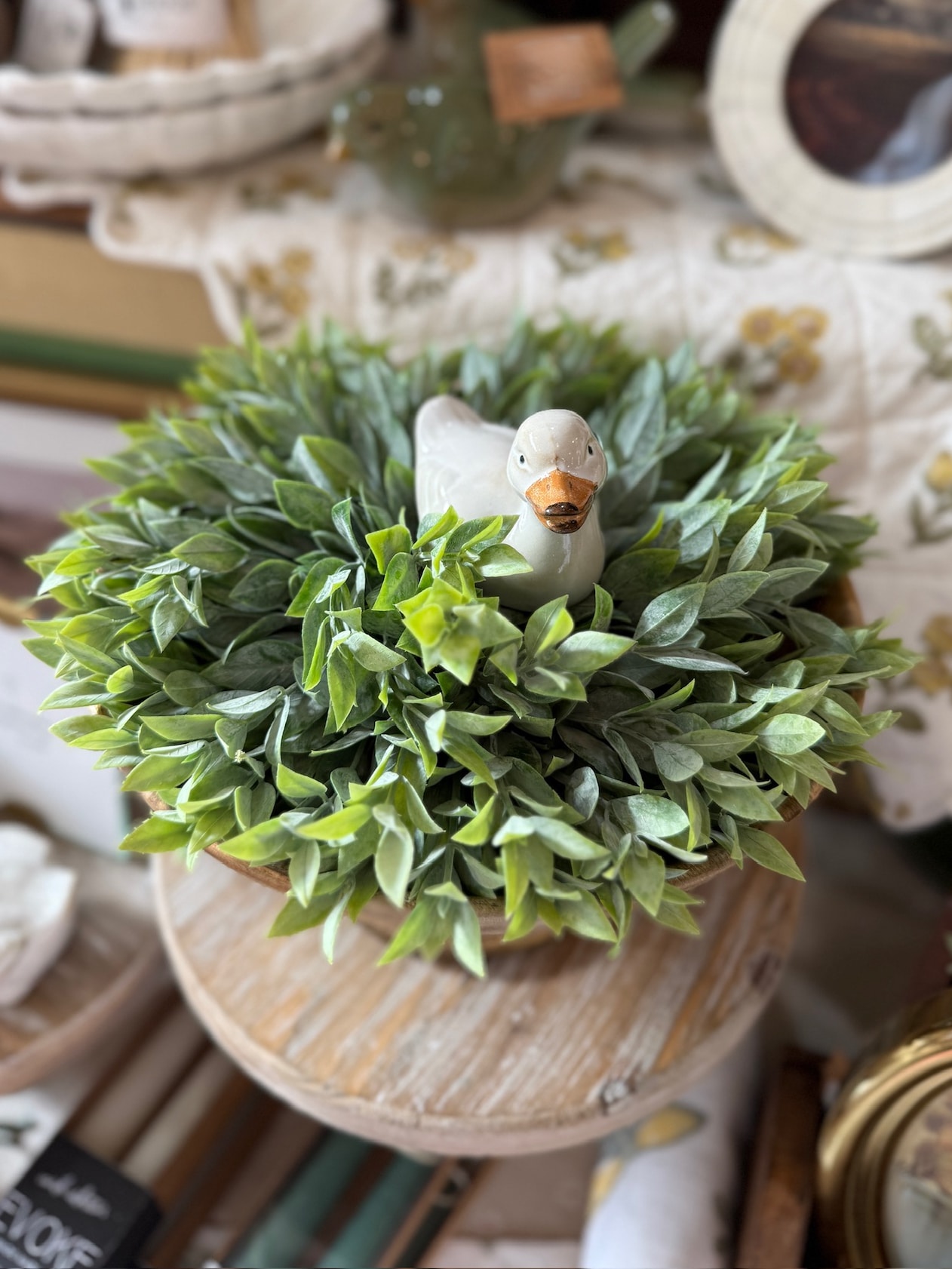 Close-up of faux powdered greenery half-sphere with a small white ceramic duck figurine nestled in the center, displayed on a wooden pedestal.