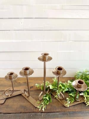 Foldable gold candle holder with floral-inspired cups displayed on wooden surface with greenery