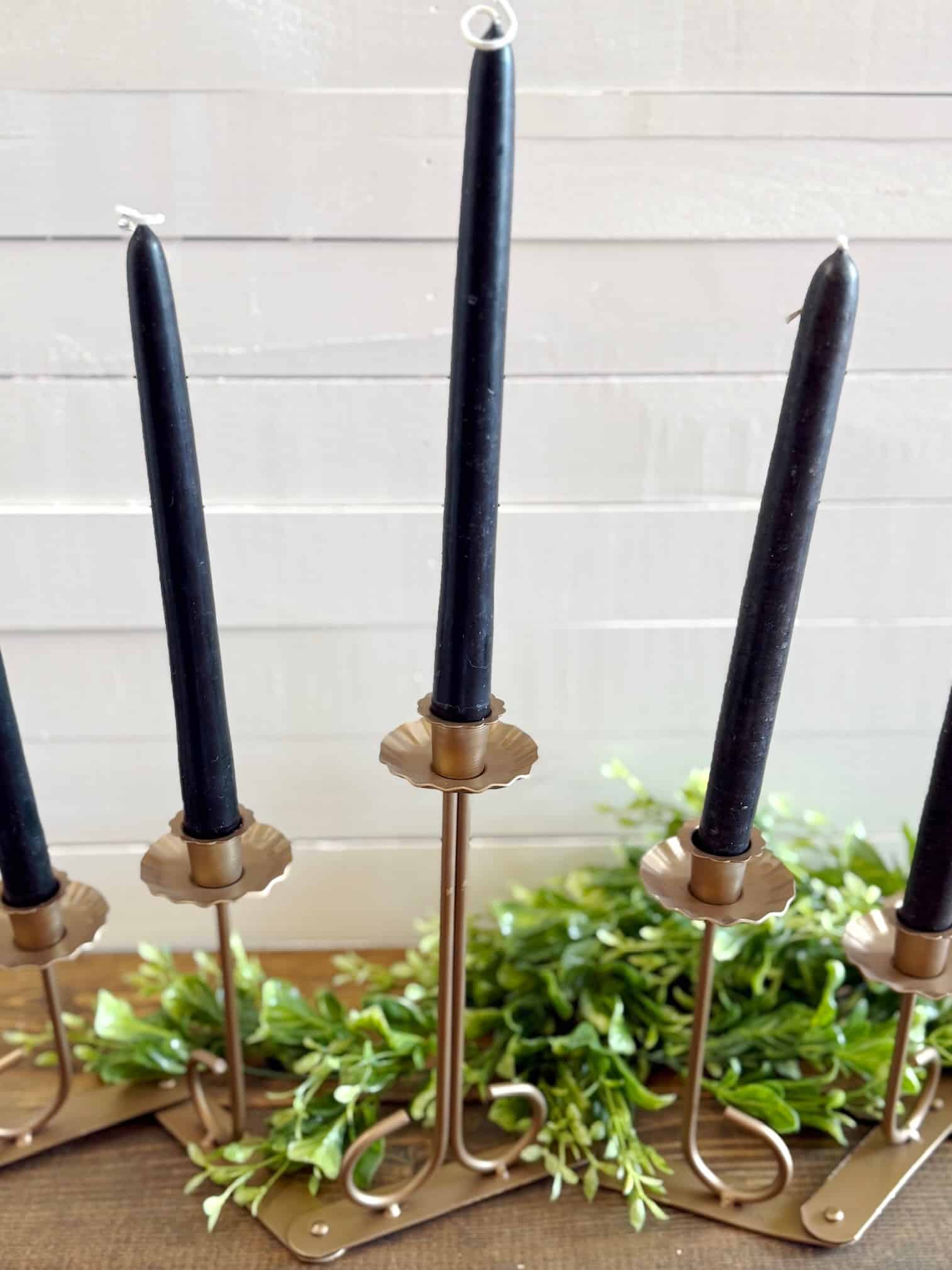 Gold foldable candle holder styled with black taper candles and green accents