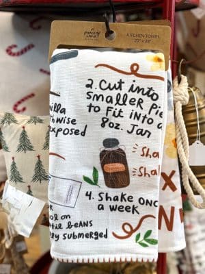 Illustrated vanilla extract recipe kitchen towel showing handwritten steps, vanilla bean graphics, a bottle, and playful doodles.