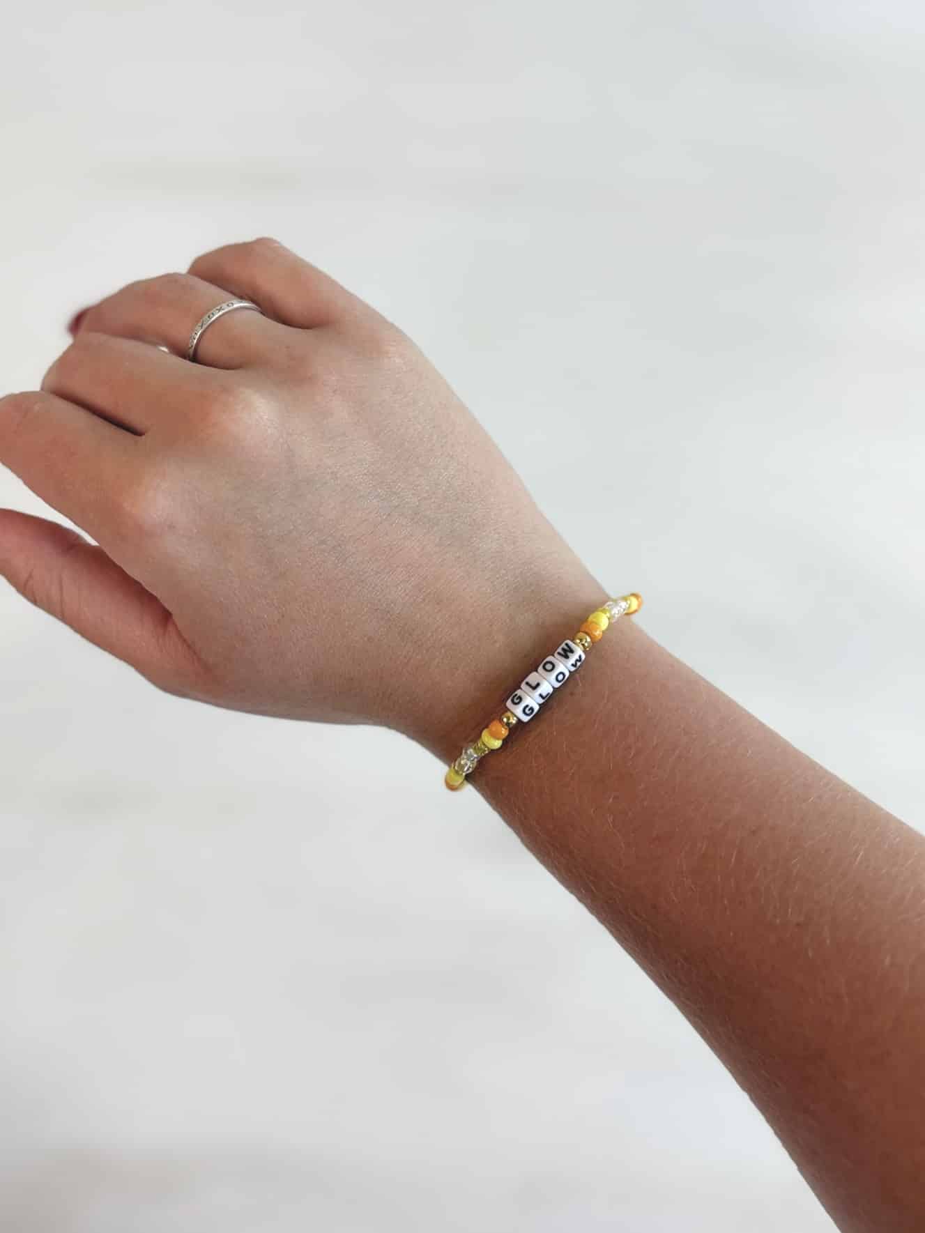 Single-strand bracelet with yellow beads and the word GLOW in block letters, styled on wrist.